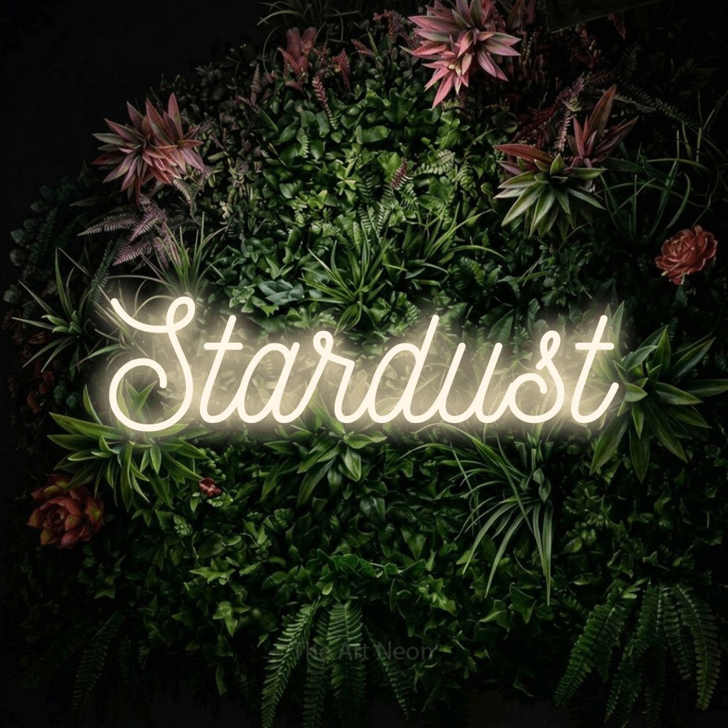 Warm white script-style LED neon sign reading "Stardust" against a flowering garden wall for bedroom décor