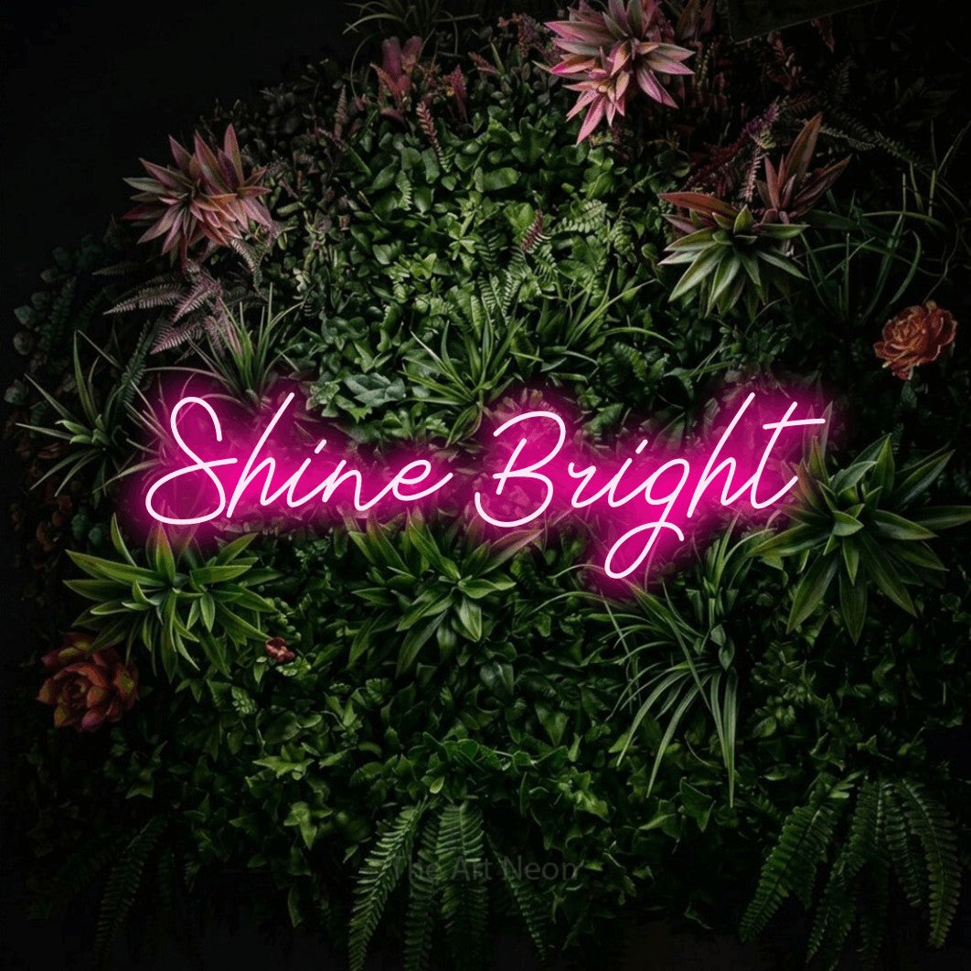 Hot pink script-style LED neon sign reading "Shine Bright" against a flowering garden wall for bedroom décor