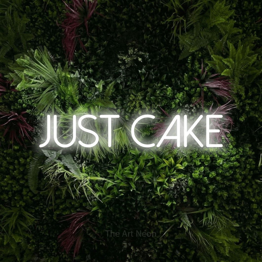 Cool white LED neon sign reading "Just Cake" against a lush garden wall with pink flowers for kitchen décor