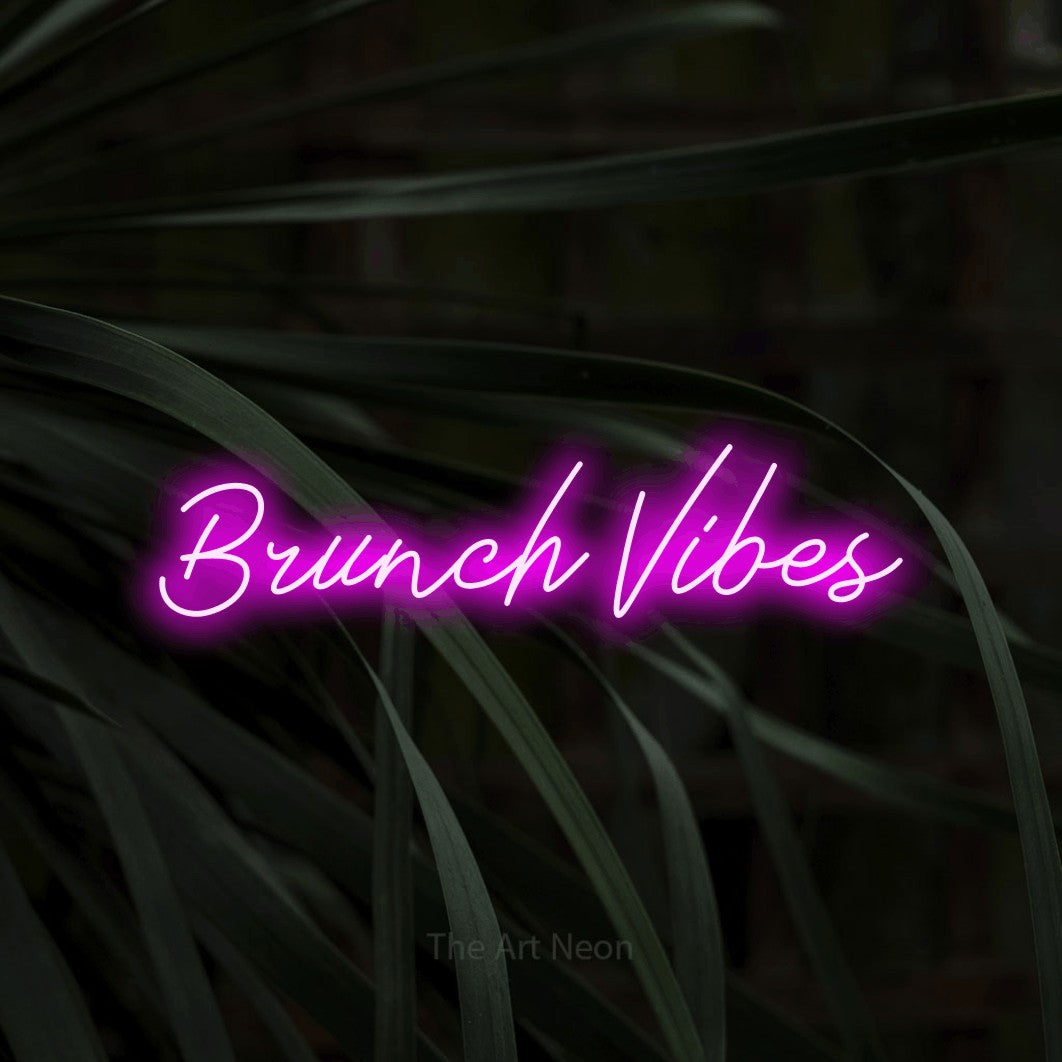 Pink script-style LED neon sign reading "Brunch Vibes" against dark tropical leaves for kitchen décor
