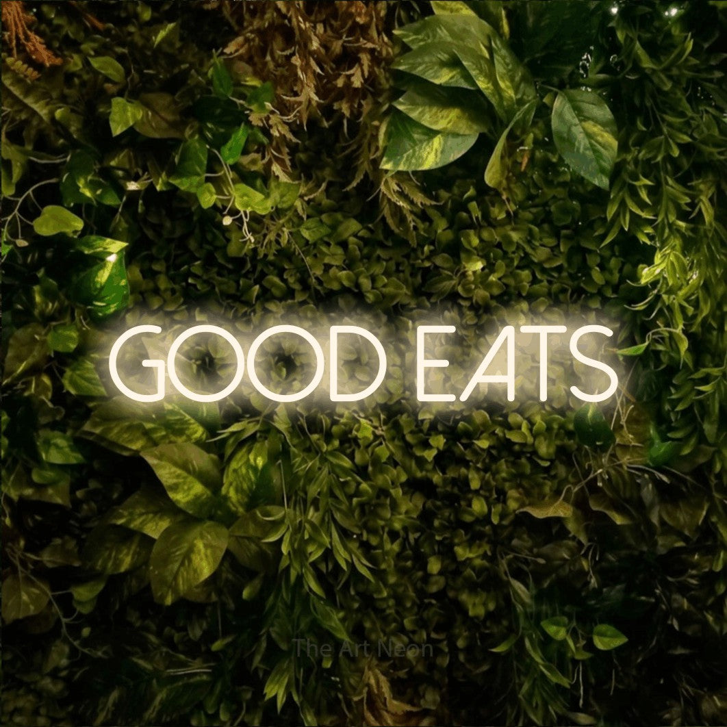 Warm white LED neon sign reading "Good Eats" against a textured moss and foliage wall for kitchen décor