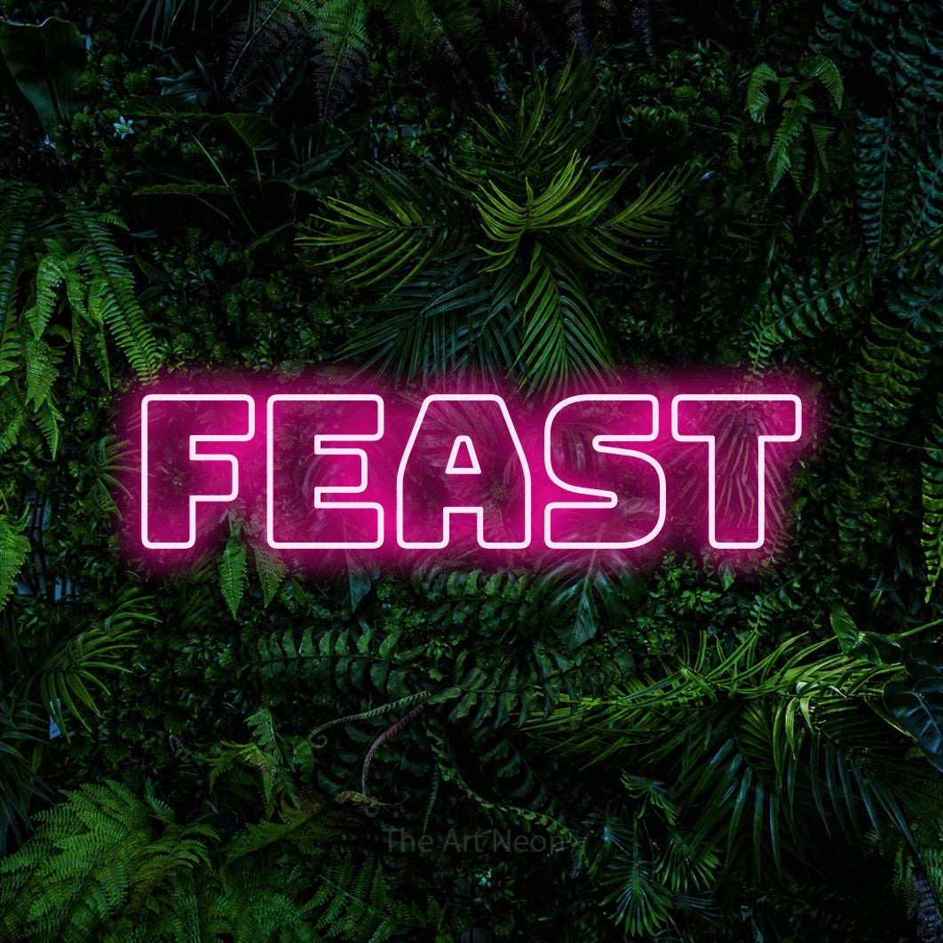 Hot pink outline-style LED neon sign reading "Feast" against a dense tropical foliage wall for kitchen décor