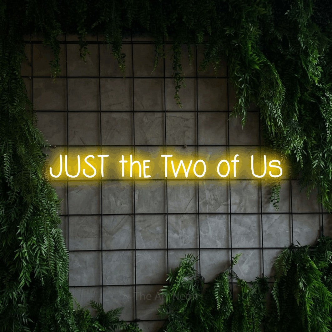 Yellow LED neon sign reading "Just the Two of Us" against a green grid wall with foliage