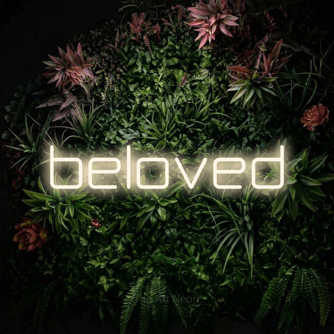 Warm white LED neon sign reading "Beloved" against a flowering garden wall
