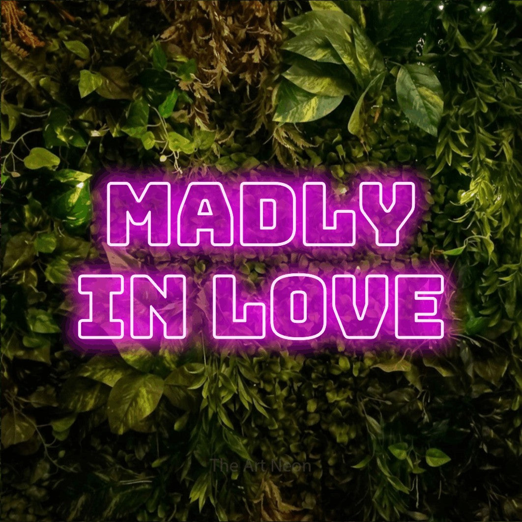 Pink outline-style LED neon sign reading "Madly in Love" against a textured moss and foliage wall