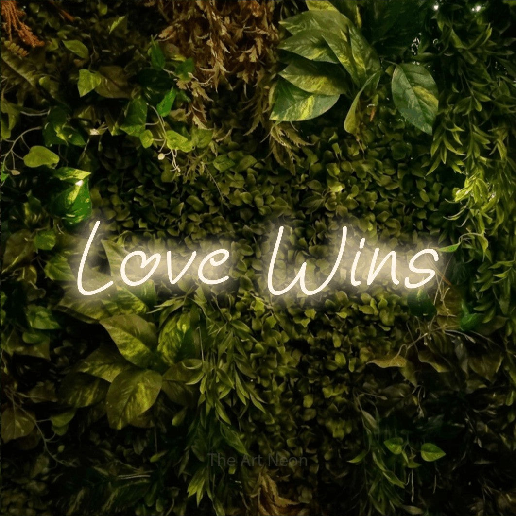 Warm white LED neon sign reading "Love Wins" against a textured moss and foliage wall