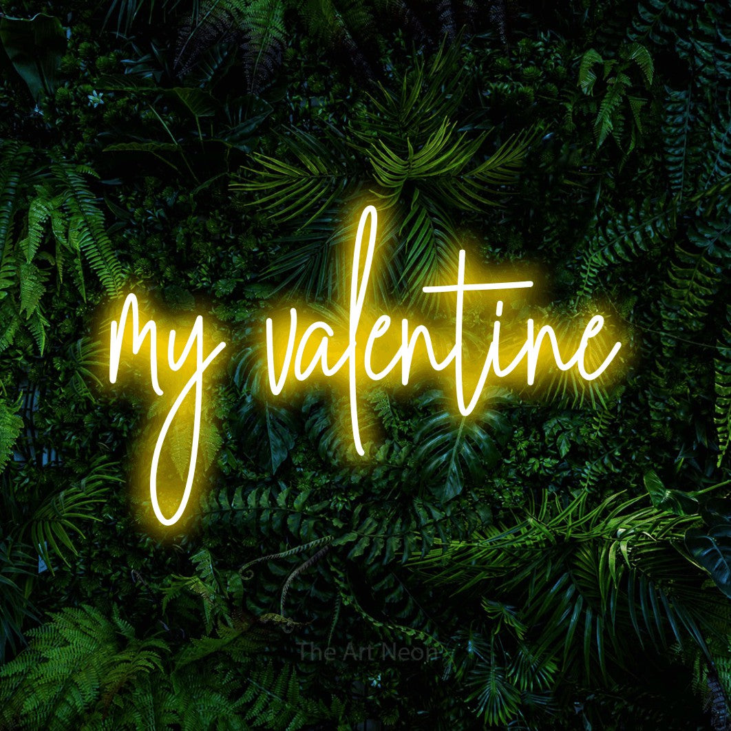 Yellow script-style LED neon sign reading "My Valentine" against a dense tropical foliage wall