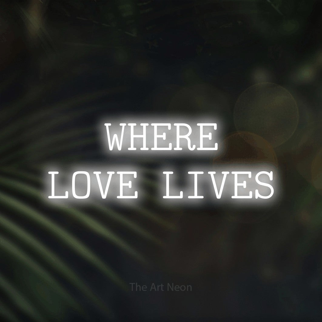 Cool white LED neon sign reading "Where Love Lives" against dark blurred palm leaves