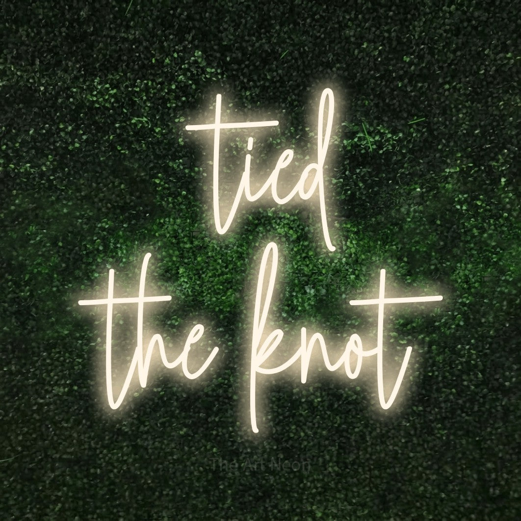 Warm white script-style LED neon sign reading "Tied the Knot" against a textured green moss wall for wedding décor