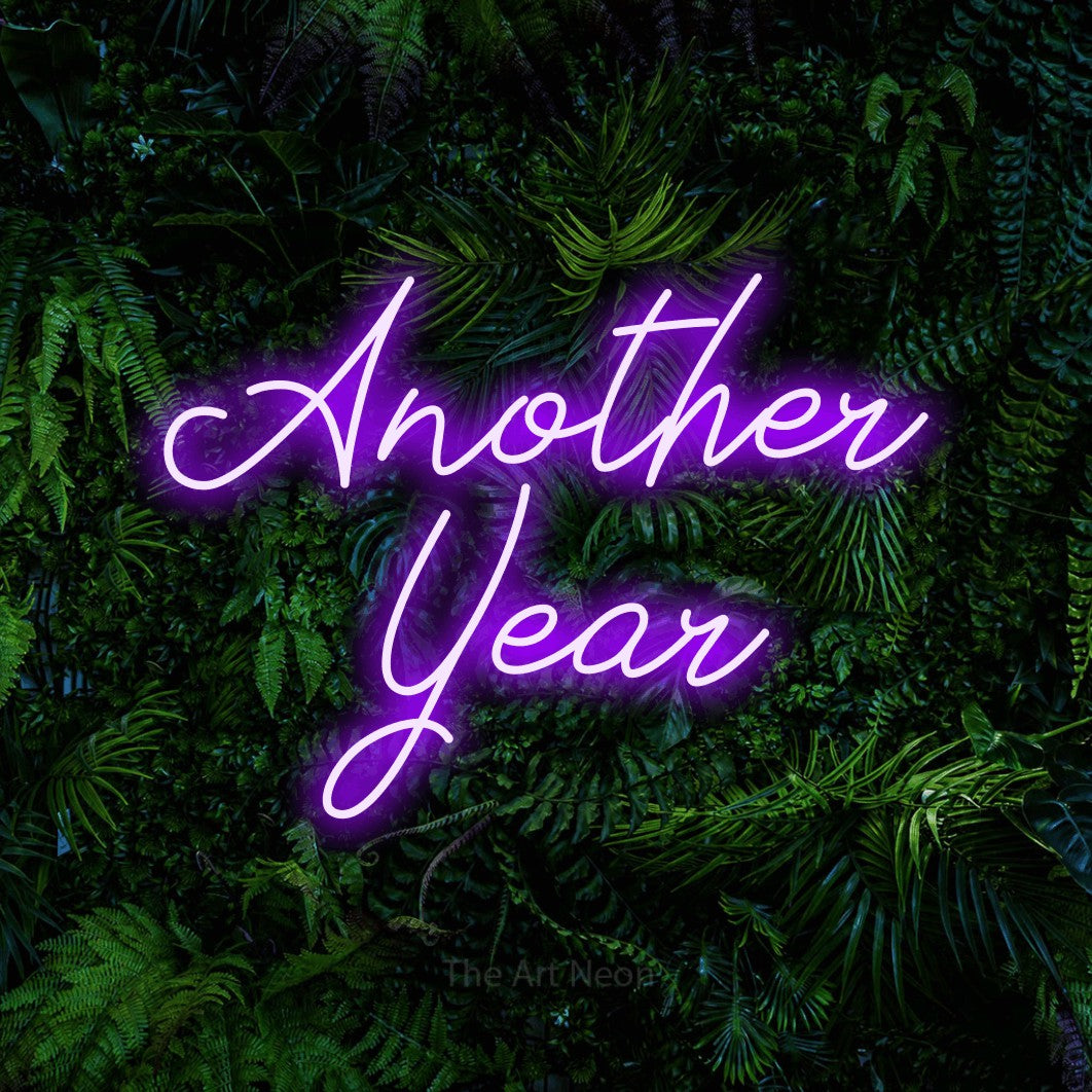 Purple script-style LED neon sign reading "Another Year" against a dense tropical foliage wall for party décor