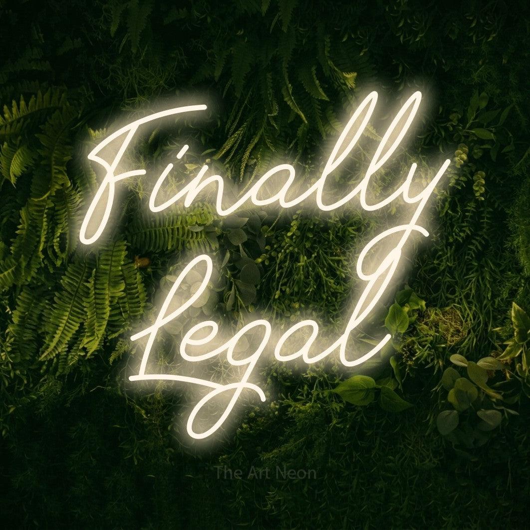 Warm white script-style LED neon sign reading "Finally Legal" against a moss-covered green wall for party décor
