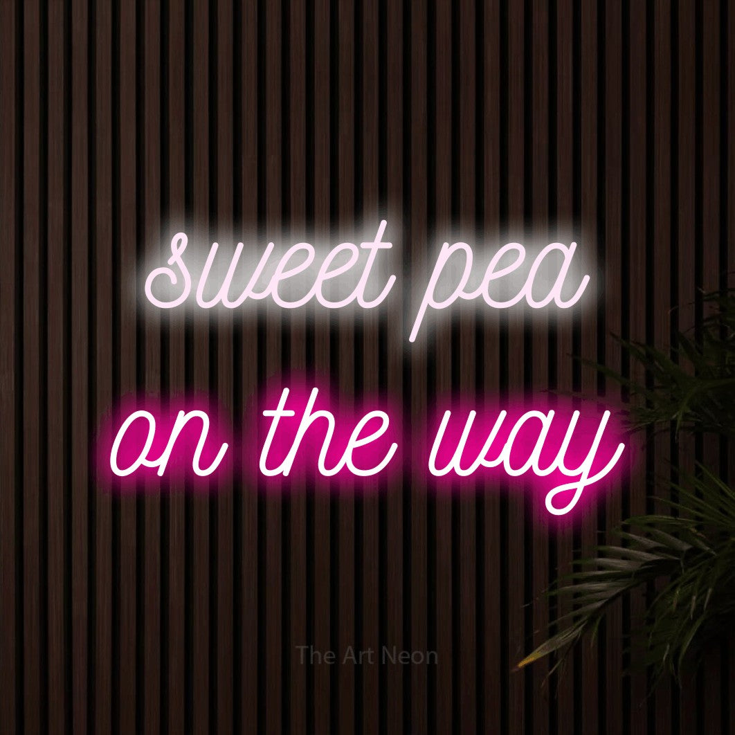 Hot pink and cool white script-style LED neon sign reading "Sweet Pea on the Way" against dark wooden slats