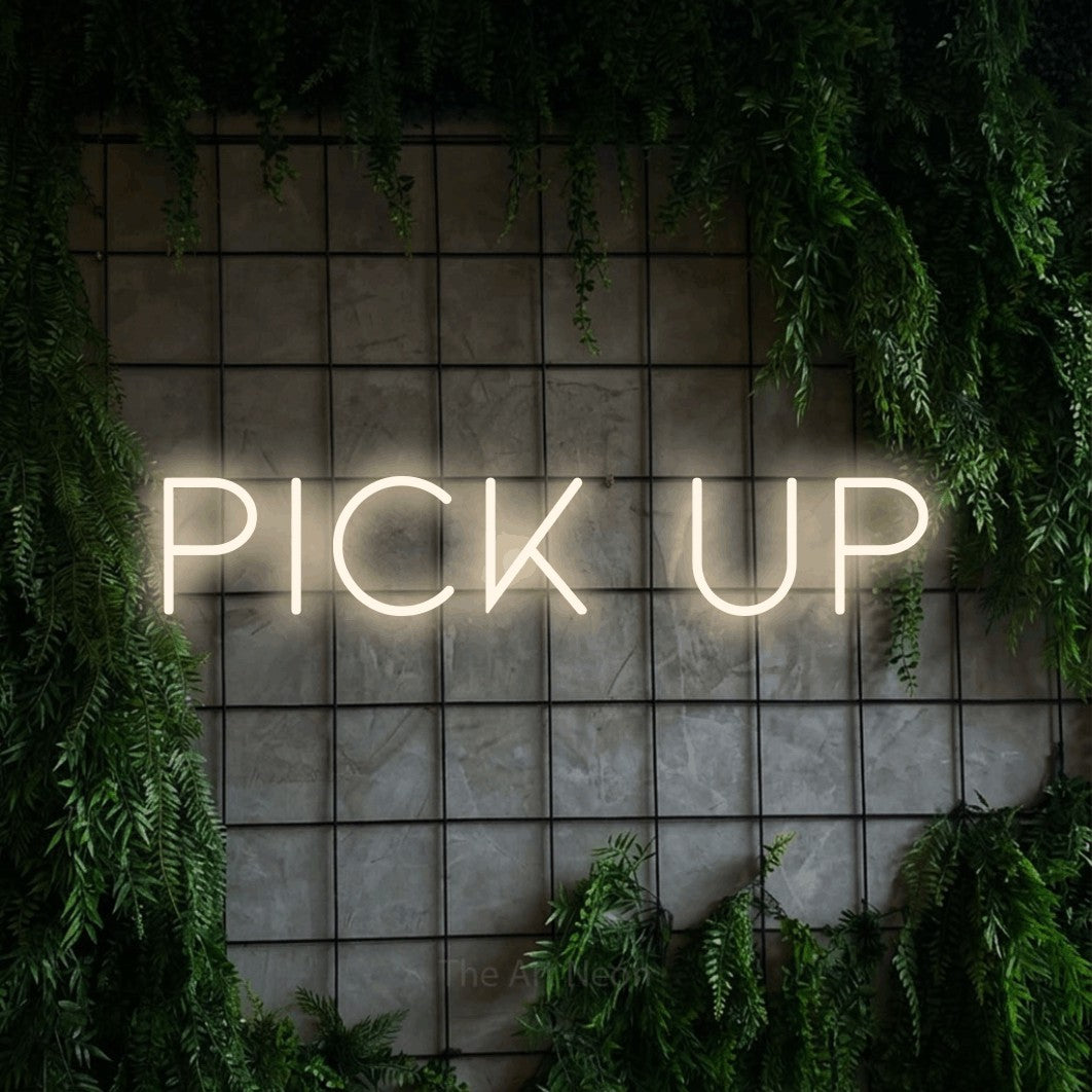 Warm white LED neon sign reading "Pick Up" against a green grid wall with foliage for restaurant décor