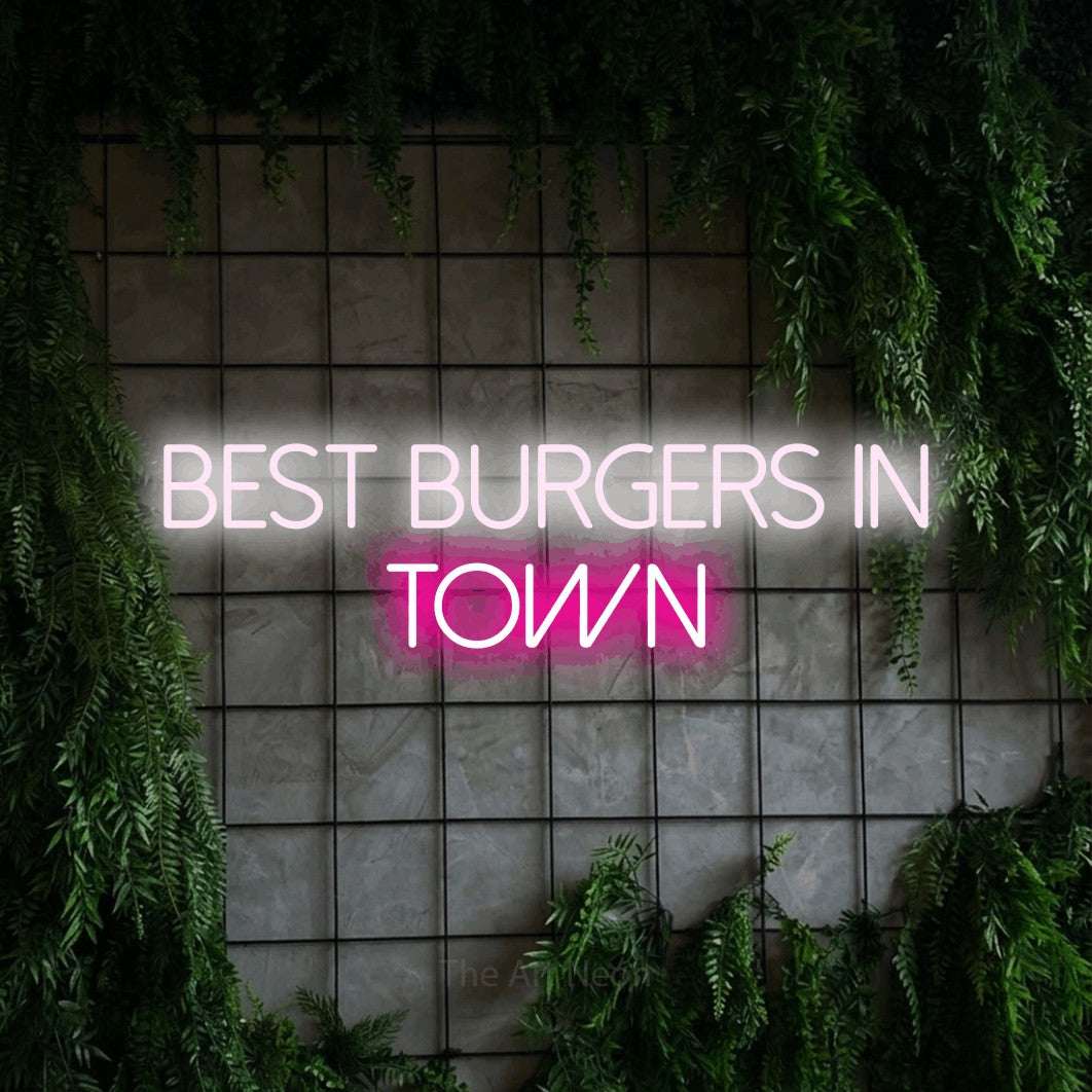 Hot pink and cool white LED neon sign reading "Best Burgers in Town" against a green grid wall with foliage