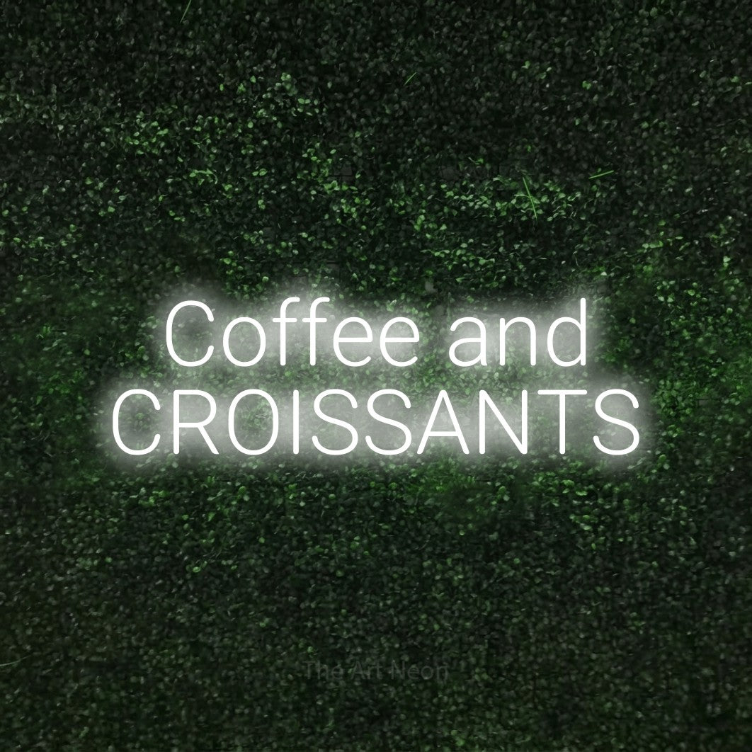 Cool white LED neon sign reading "Coffee and Croissants" against a textured green moss wall for café décor