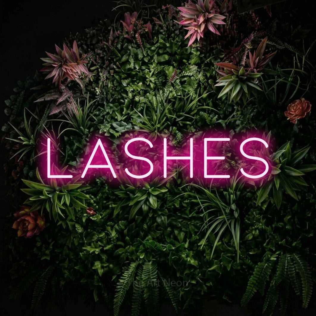 Hot pink LED neon sign reading "Lashes" against a flowering garden wall for salon décor