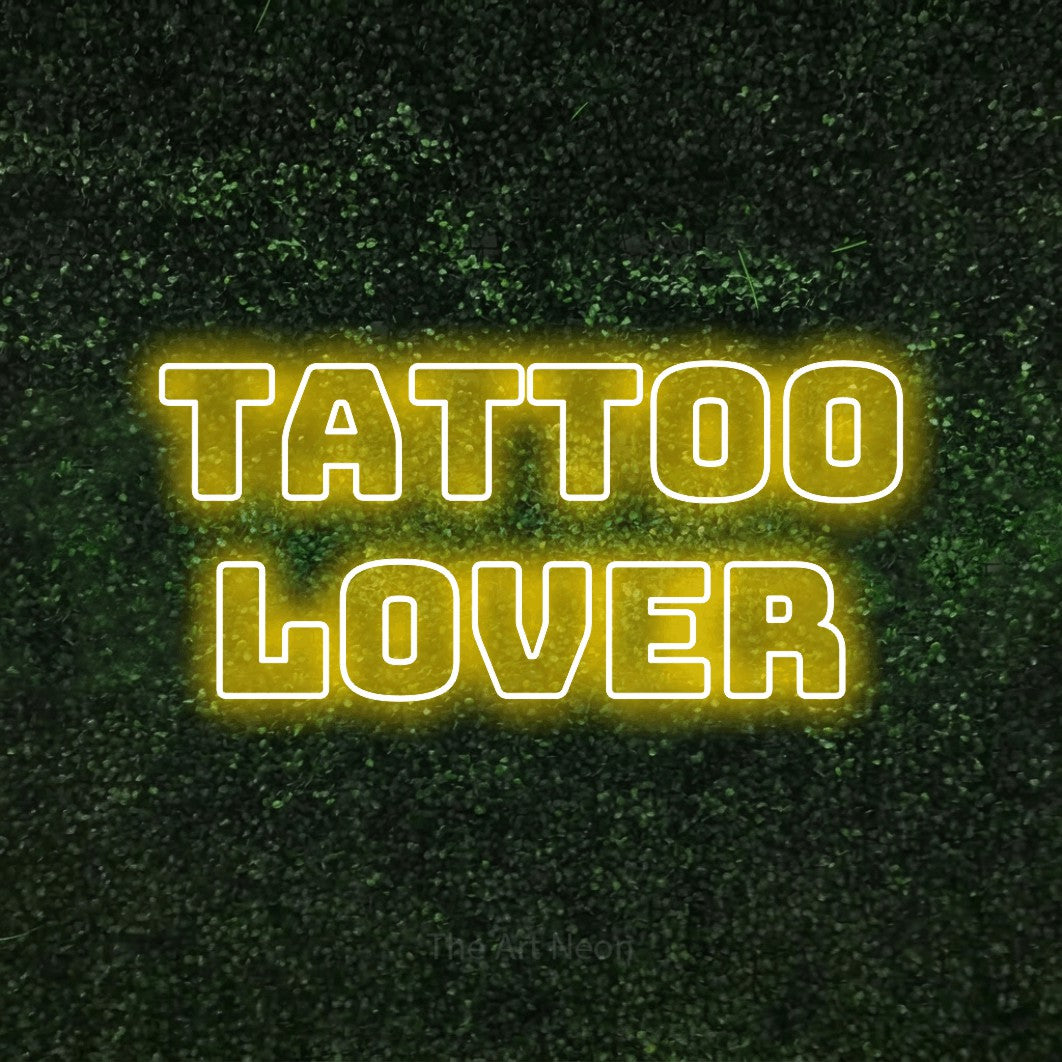 Yellow outline-style LED neon sign reading "Tattoo Lover" against a textured green moss wall for tattoo studio décor
