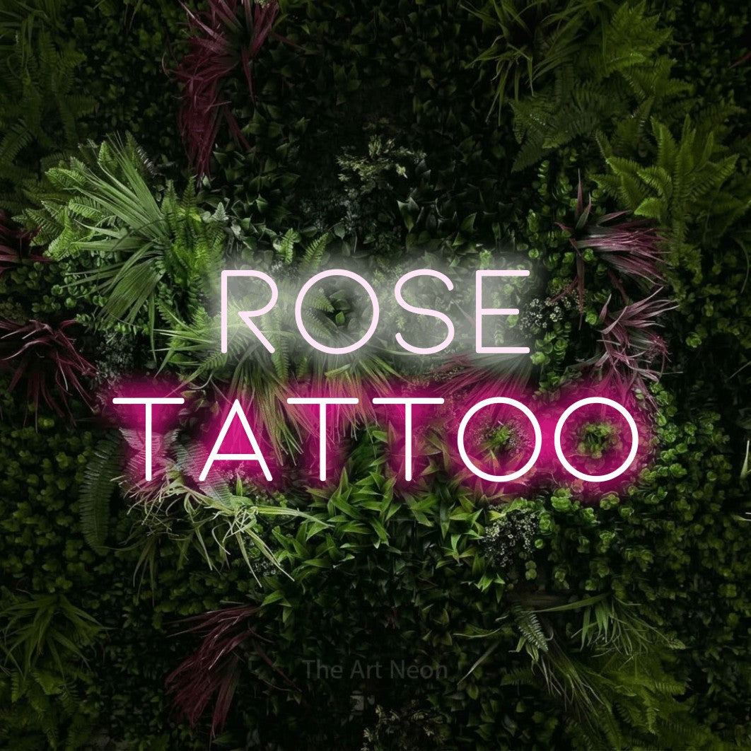 Hot pink and cool white LED neon sign reading "Rose Tattoo" against a lush garden wall with pink flowers