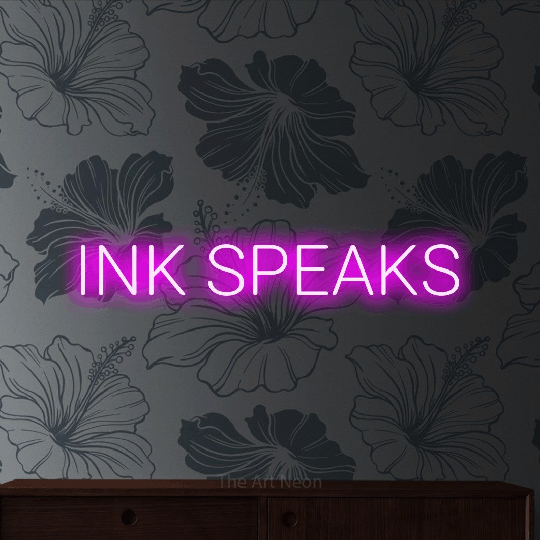 Enseigne néon à DEL à lumière rose, affichant « Ink Speaks » sur un papier peint floral gris, pour décorer un studio de tatouage
