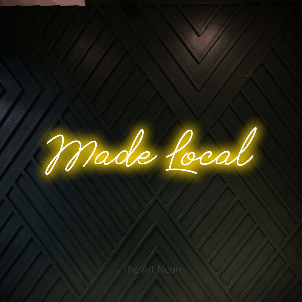 Yellow script-style LED neon sign reading "Made Local" against a dark geometric wood wall