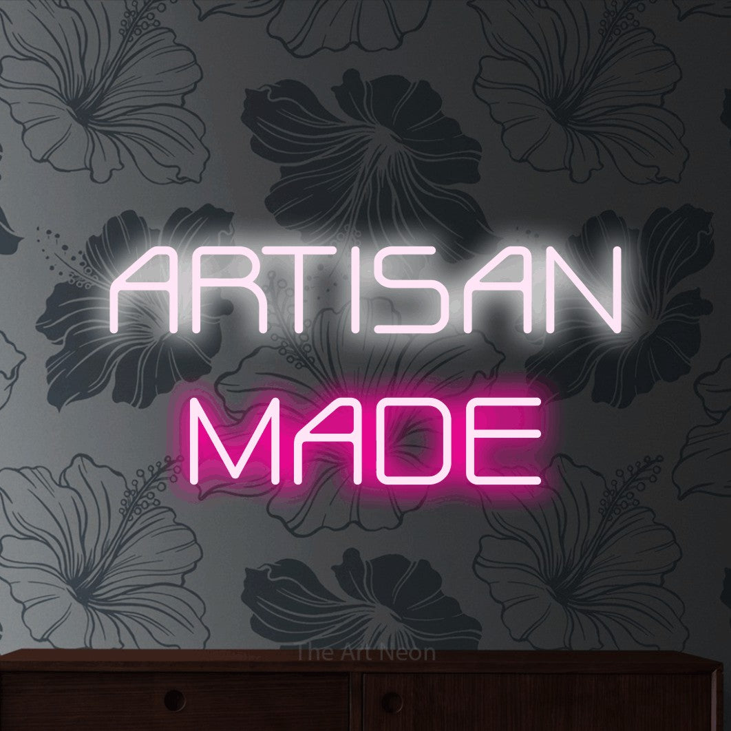 Hot pink and cool white LED neon sign reading "Artisan Made" against grey floral wallpaper