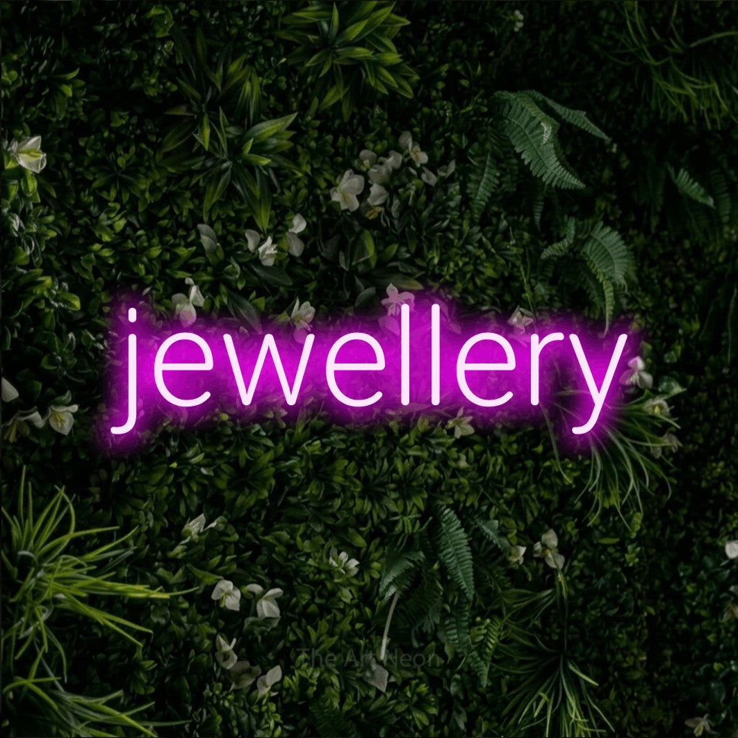 Pink LED neon sign reading "Jewellery" against a leafy green wall