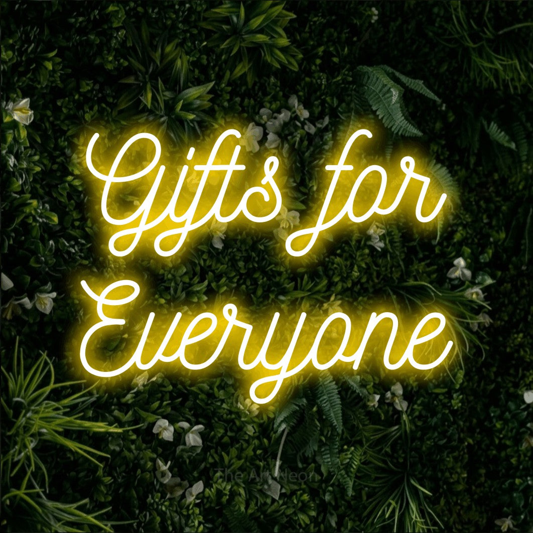 Yellow script-style LED neon sign reading "Gifts for Everyone" against a leafy green wall