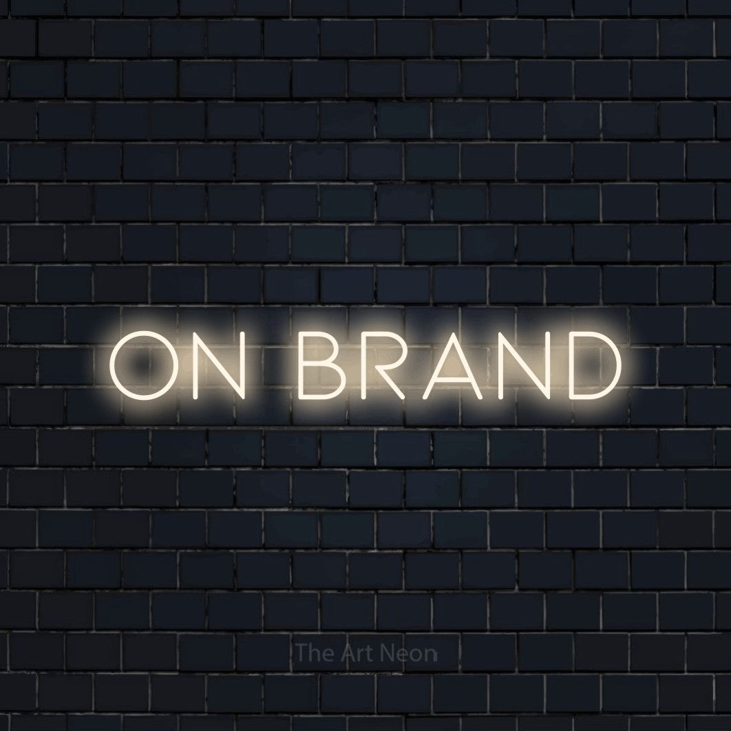 Warm white LED neon sign reading "On Brand" against a dark navy brick wall for office décor