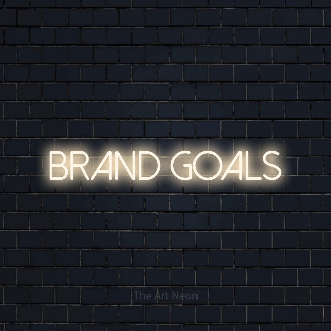 Warm white LED neon sign reading "Brand Goals" against a dark navy brick wall for office décor