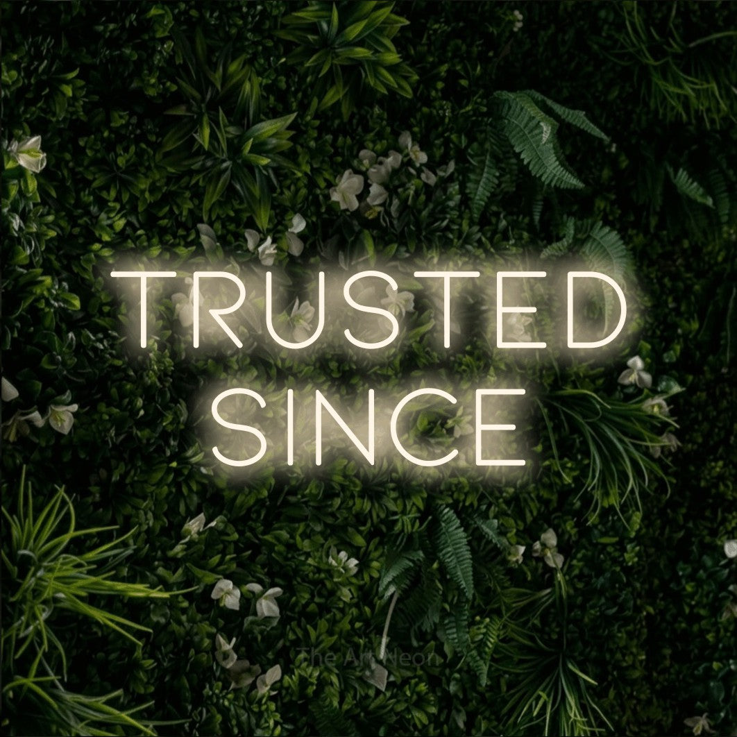 Warm white LED neon sign reading "Trusted Since" against a leafy green wall for office décor