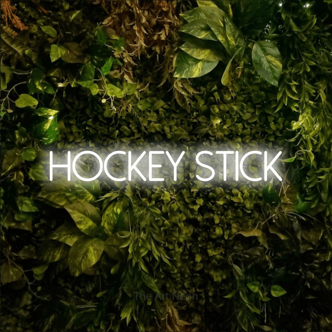 Cool white LED neon sign reading "Hockey Stick" against a textured moss and foliage wall