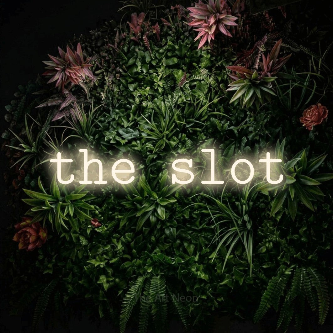 Warm white LED neon sign reading "The Slot" against a flowering garden wall