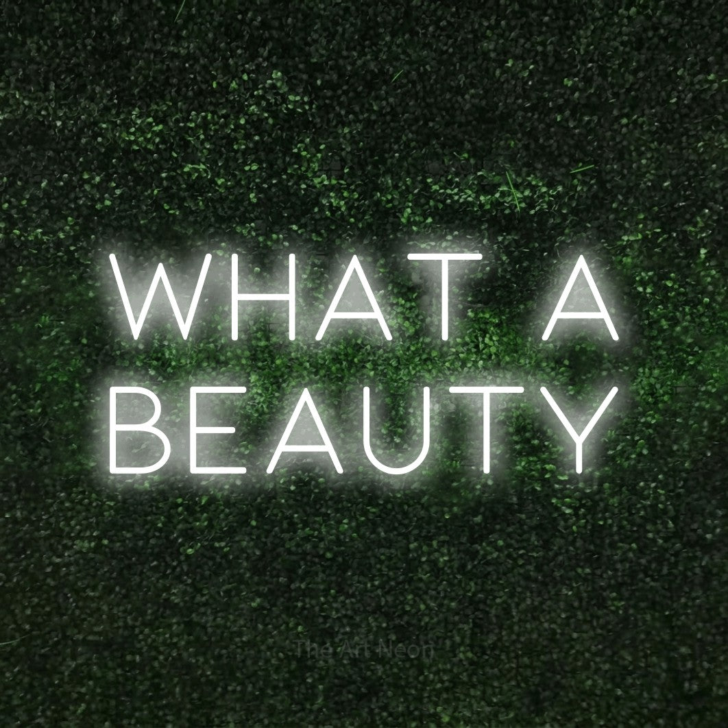Cool white LED neon sign reading "What a Beauty" against a textured green moss wall