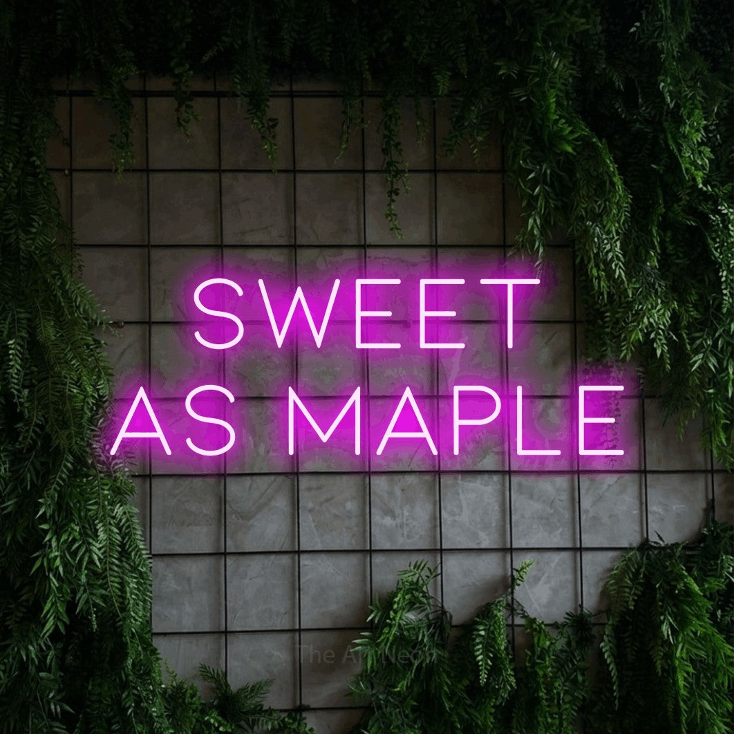 Pink LED neon sign reading "Sweet as Maple" against a green grid wall with foliage