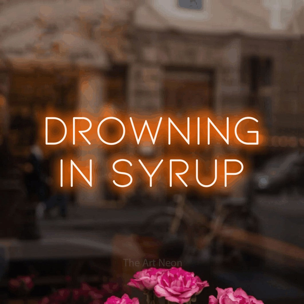 Orange LED neon sign reading "Drowning in Syrup" in a softly blurred café interior