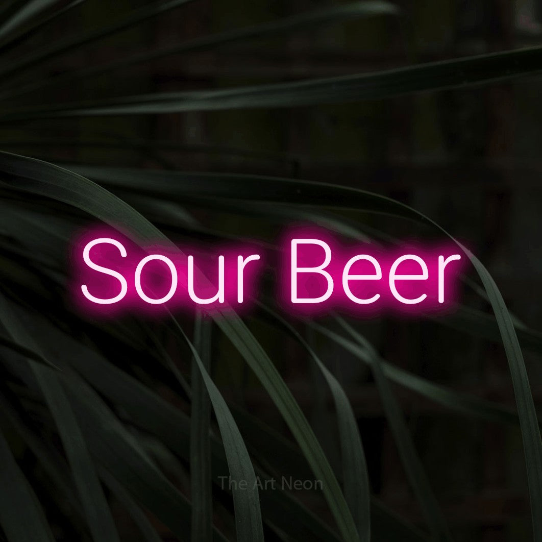 Hot pink LED neon sign reading "Sour Beer" against dark tropical leaves
