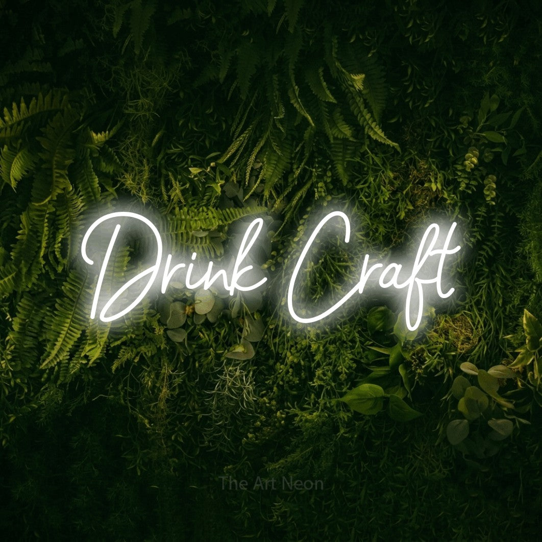 Cool white script-style LED neon sign reading "Drink Craft" against a moss-covered green wall