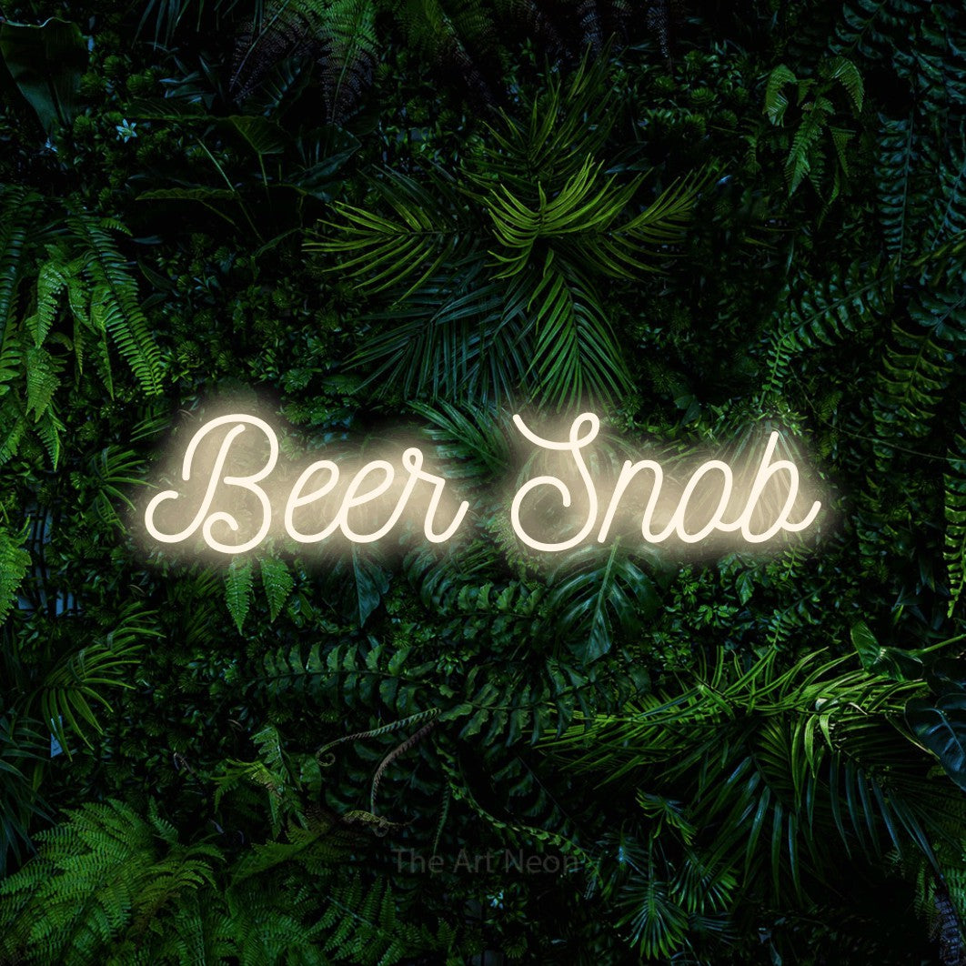 Warm white script-style LED neon sign reading "Beer Snob" against a dense tropical foliage wall