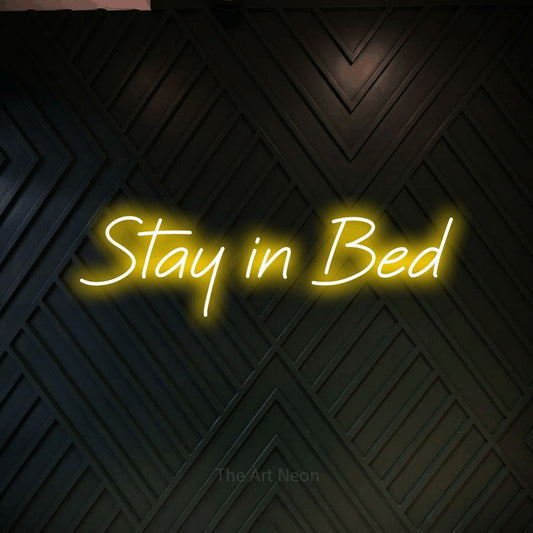 Yellow LED neon sign reading "Stay in Bed" against a dark geometric wood wall for bedroom décor