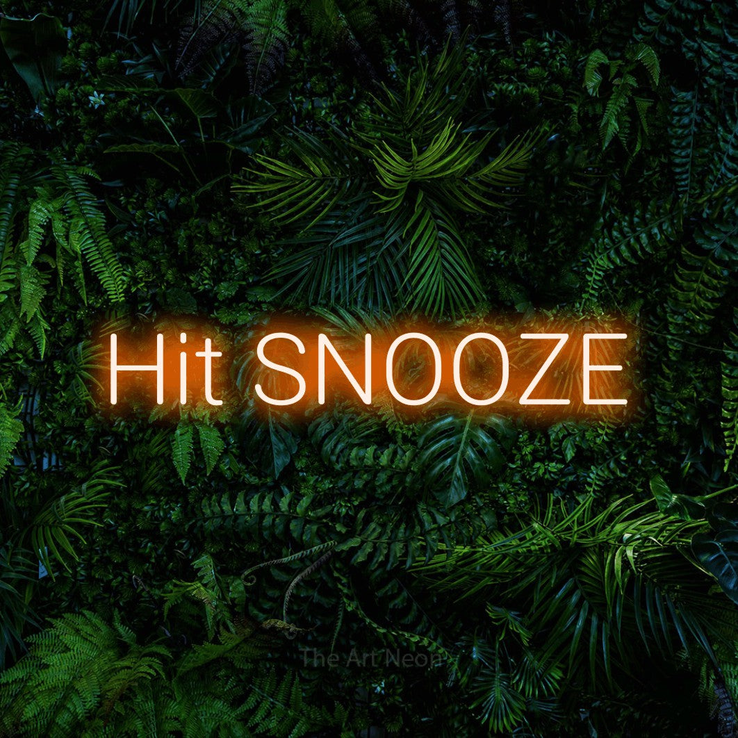 Orange LED neon sign reading "Hit Snooze" against a dense tropical foliage wall for bedroom décor
