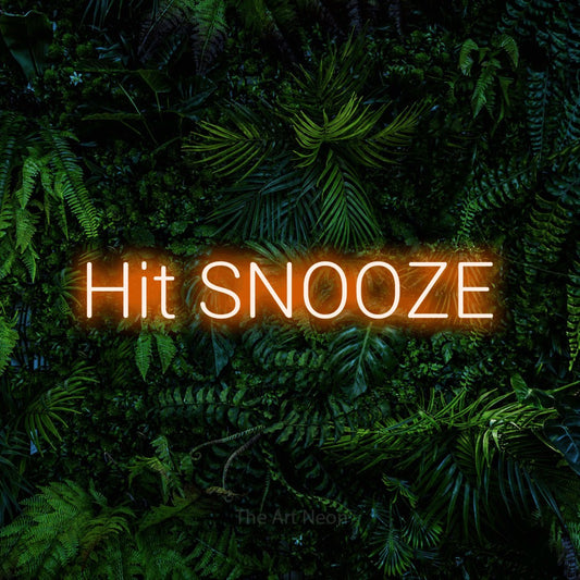 Orange LED neon sign reading "Hit Snooze" against a dense tropical foliage wall for bedroom décor