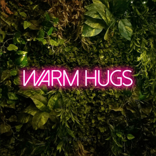 Hot pink LED neon sign reading "Warm Hugs" against a textured moss and foliage wall for bedroom décor
