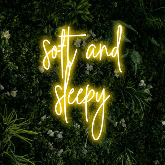 Yellow script-style LED neon sign reading "Soft and Sleepy" against a leafy green wall for bedroom décor