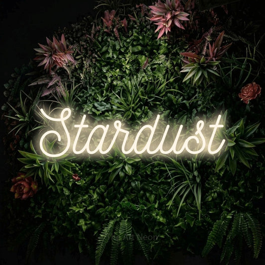 Warm white script-style LED neon sign reading "Stardust" against a flowering garden wall for bedroom décor