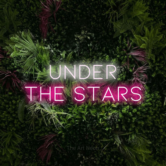 Hot pink and cool white LED neon sign reading "Under the Stars" against a lush garden wall with pink flowers