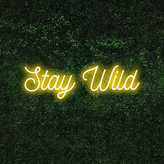 Yellow script-style LED neon sign reading "Stay Wild" against a textured green moss wall for bedroom décor
