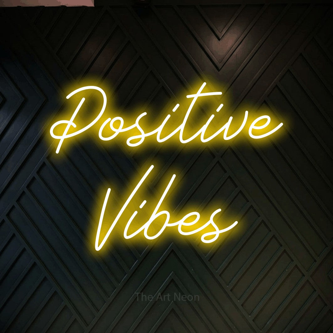 Yellow script-style LED neon sign reading "Positive Vibes" against a dark geometric wood wall for bedroom décor