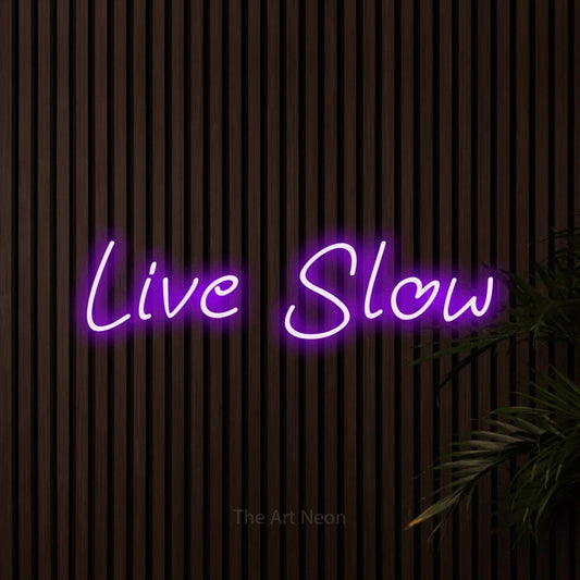Purple LED neon sign reading "Live Slow" against dark wooden slats for bedroom décor