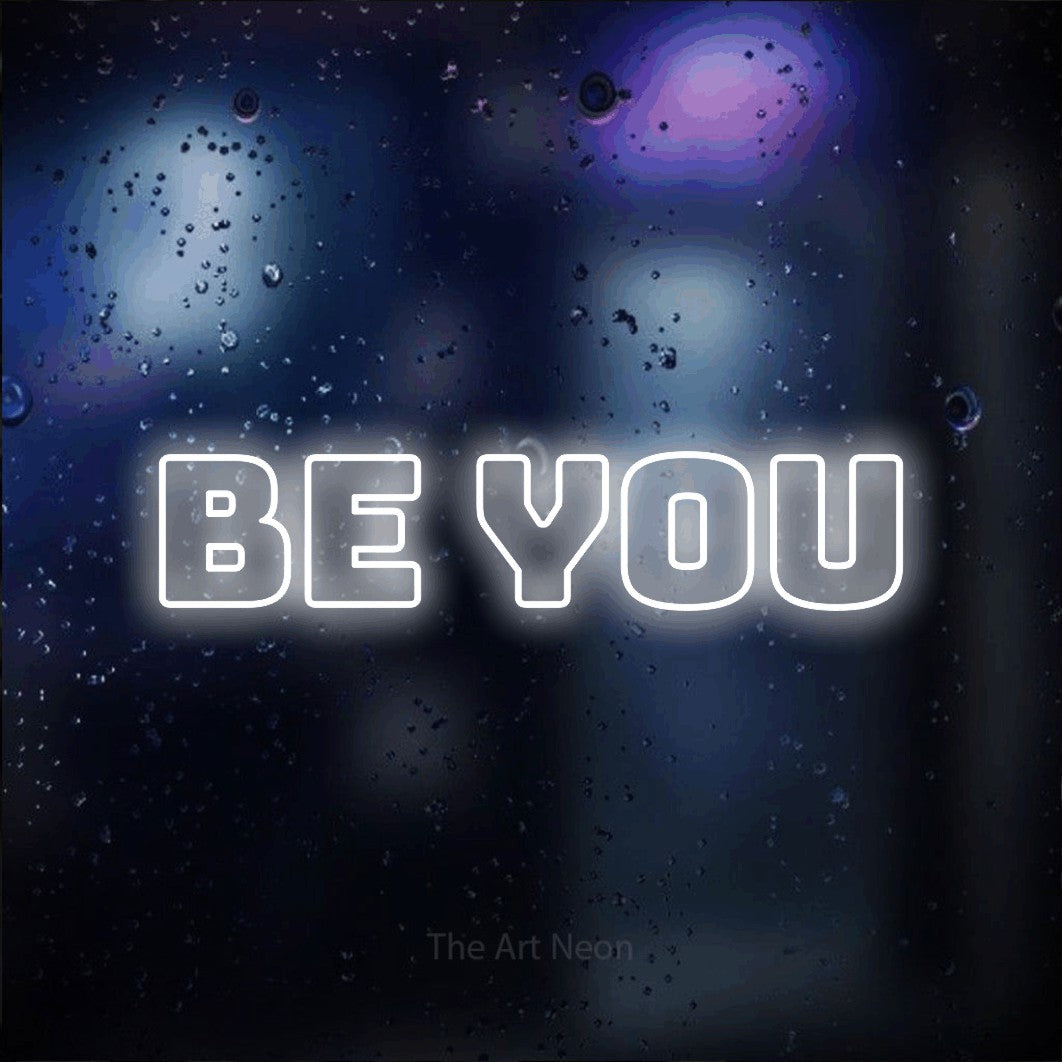 Cool white outline-style LED neon sign reading "Be You" against a dark blue bokeh background for bedroom décor