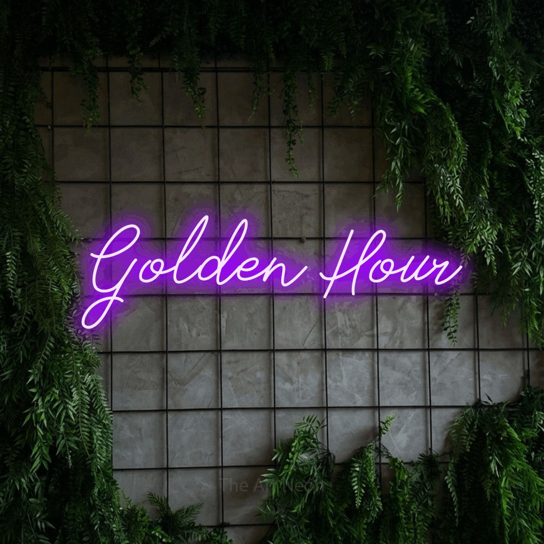 Purple script-style LED neon sign reading "Golden Hour" against a green grid wall with foliage for bedroom décor